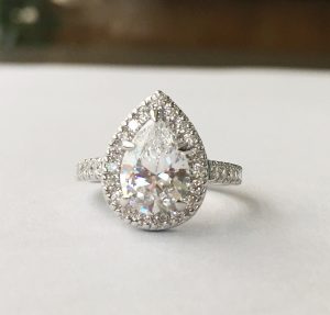 stunning antique style tear drop halo engagement ring showing large diamond surrounded by 12 smaller diamonds on a half band of 5 more smaller diamond simulants on either side