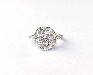 stunning antique style halo engagement ring showing large diamond surrounded by 12 smaller diamonds on a half band of 5 more smaller diamond simulants on either side