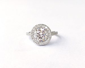 stunning antique style halo engagement ring showing large diamond surrounded by 12 smaller diamonds on a half band of 5 more smaller diamond simulants on either side